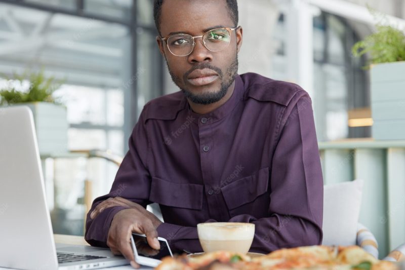 Cropped shot of handsome dark skinned man wears round spectacles and formal shirt, uses modern technologies for work Free Photo