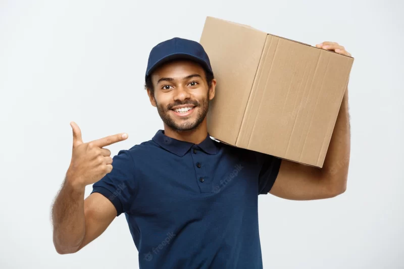 Delivery concept – portrait of happy african american delivery man pointing hand to present a box package. isolated on grey studio background. copy space. Free Photo