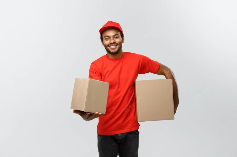 Delivery concept – portrait of happy african american delivery man in red cloth holding a box package. isolated on grey studio background. copy space. Free Photo Delivery concept – portrait of happy african american delivery man in red cloth holding a box package. isolated on grey studio background. copy space. Free Photo