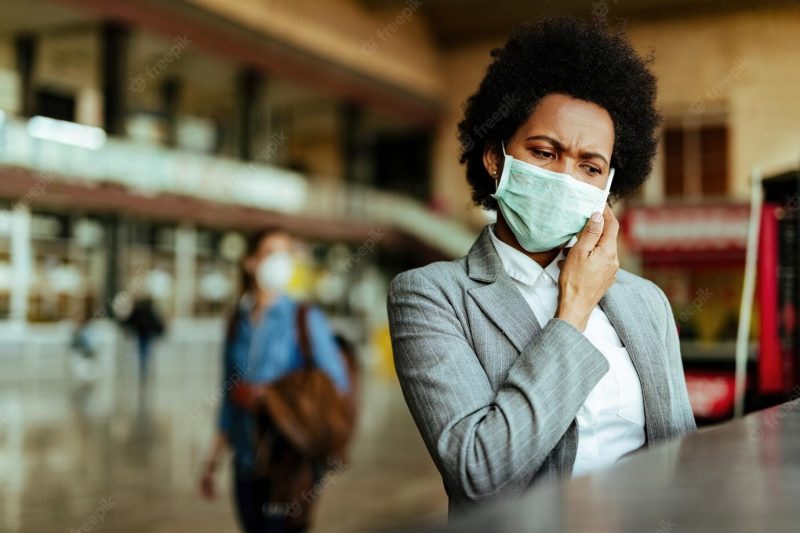 Displeased black businesswoman with protective mask on her face talking on mobile phone at airport terminal Free Photo