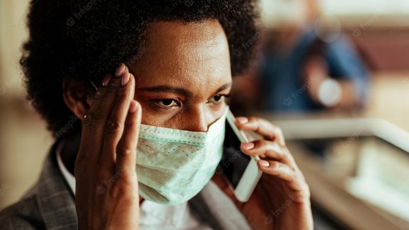 Distraught black businesswoman communicating over cell phone while wearing protective mask during virus epidemic Free Photo