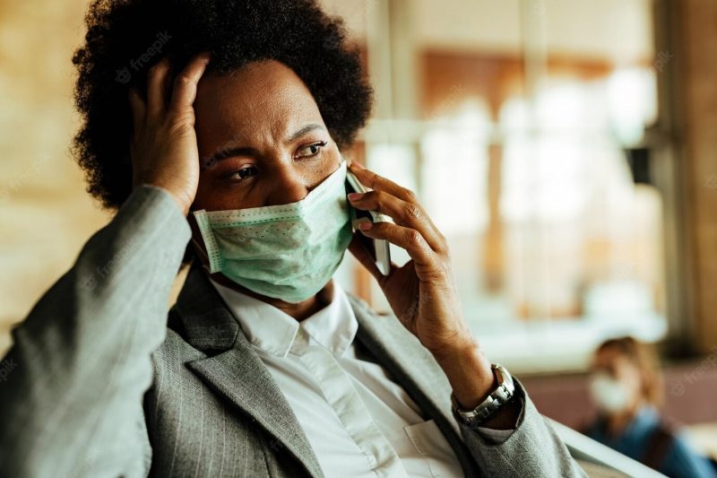 Distraught black businesswoman talking on mobile phone while wearing protective face mask at railroad station hallway Free Photo