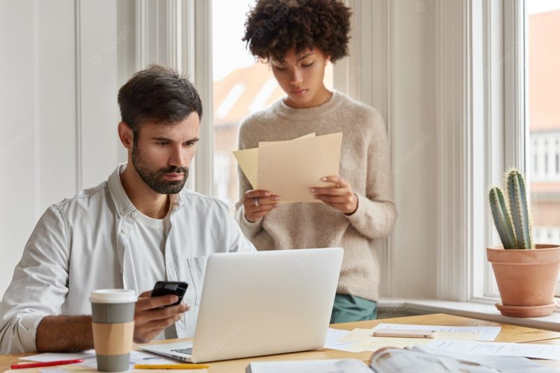 Diverse team of employees have informal meeting at domestic atmosphere, work with paper documents, develop startup during briefing. focused serious male ceo holds cell phone checks email box on laptop Free Photo