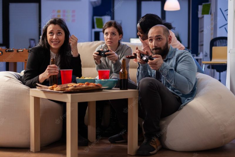 Diverse team of workers playing console game on tv at office after work using joysticks Free Photo