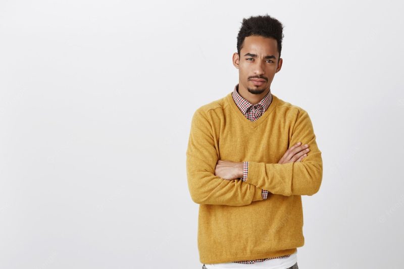 Doubt that you are telling me the truth. Suspicious serious African-American guy with Afro hairstyle crossing hands and squinting, hesitating and looking with disbelief. Free Photo