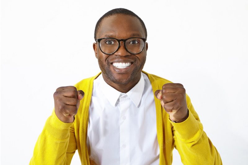 Ecstatic overjoyed young dark skinned football fan in stylish eyewear having excited look, smiling happily and clenching fists, supporting local team while watching championship, posing in studio Free Photo