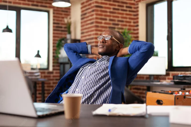 Employee sitting with hands over head to relax after finishing job at desk. business man feeling calm and peaceful, relaxing in office after working on project planning. person on break Free Photo