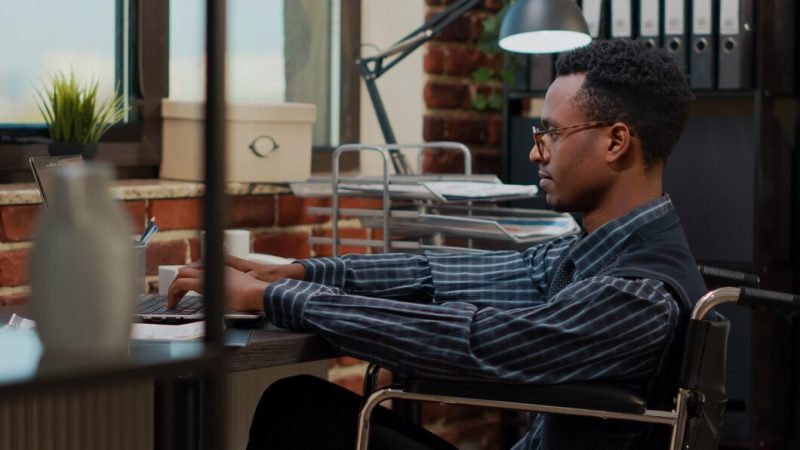 Employee with special needs working on laptop to plan strategy, using e commerce statistics. office worker sitting in wheelchair and creating financial development project on computer. Free Photo