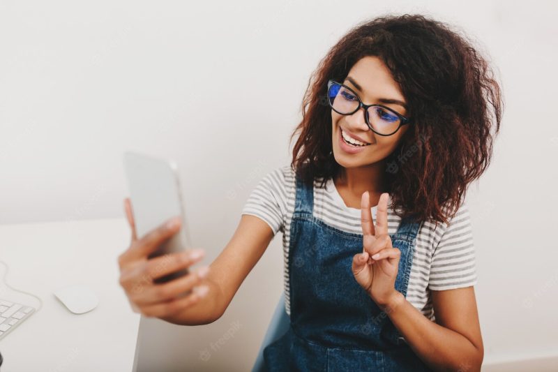 Excited black girl with pretty hairstyle taking picture of herself resting from work Free Photo