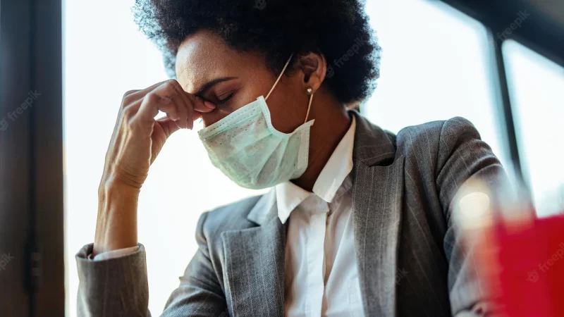 Exhausted african american businesswoman with face mask having a headache while sitting in a cafe Free Photo