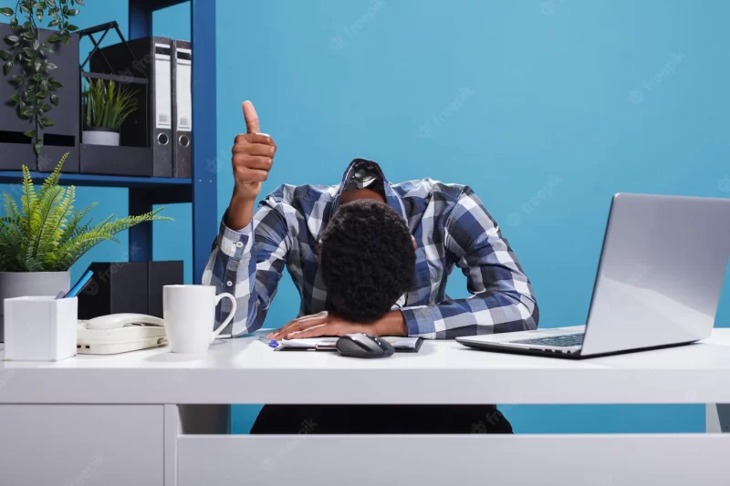 Extremely fatigued office person suffering from burnout syndrome showing thumbs up to coworkers for doing a good job. exhausted businessman falling asleep because of overwork while showing okay symbol. Free Photo