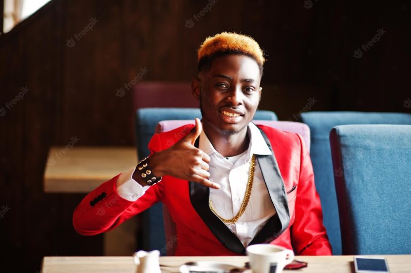 Fashion african american man model at red suit with highlights hair sitting at cafe with coffee and show finger gesture Free Photo