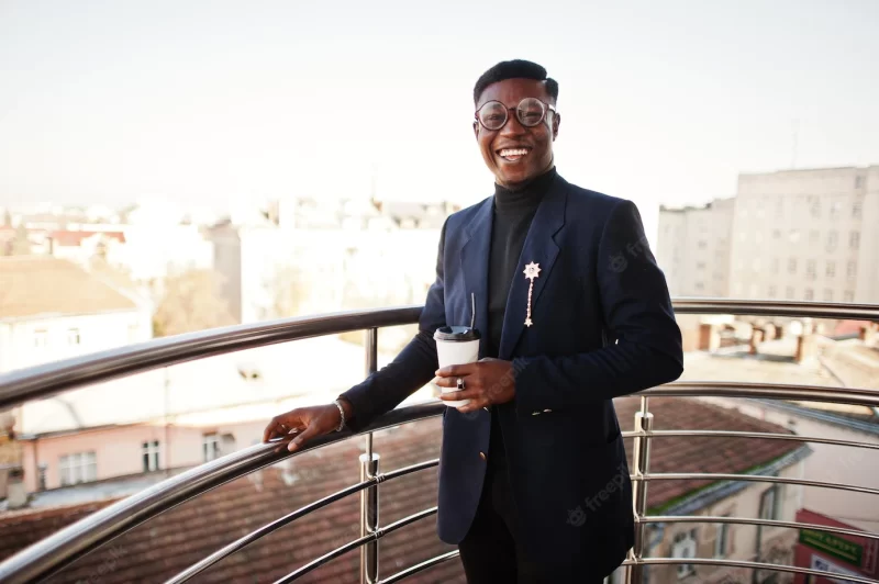 Fashionable african american man in suit and glasses with cup of coffee at hands posed on Balkony at office Free Photo