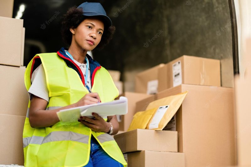 Female african american courier thinking while going through delivery schedule list in a delivery van Free Photo