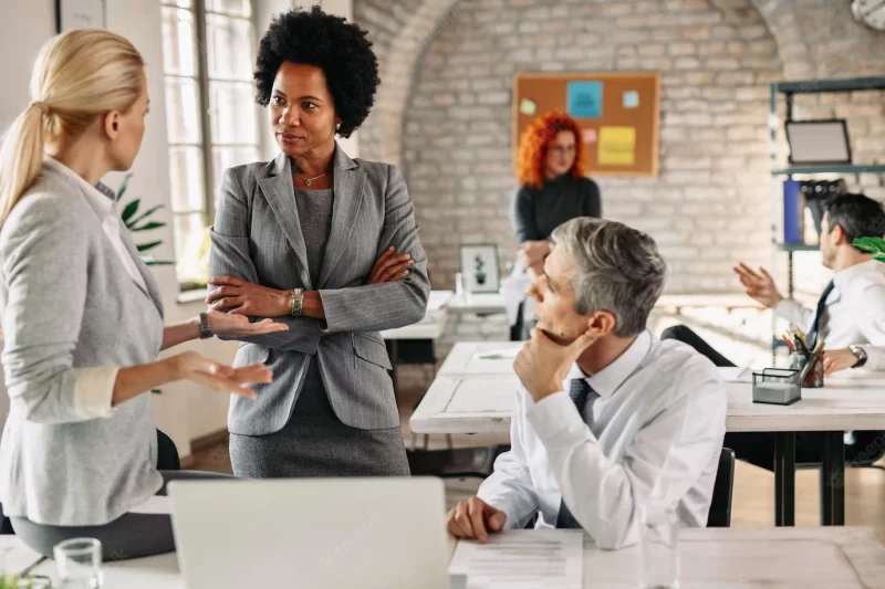 Female african american entrepreneur and her colleagues communicating on a business meeting in modern office there are people in the background Free Photo