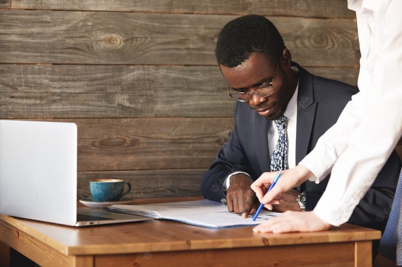 Focused African American businessman checking papers with his personal assistant in white shirt Free Photo