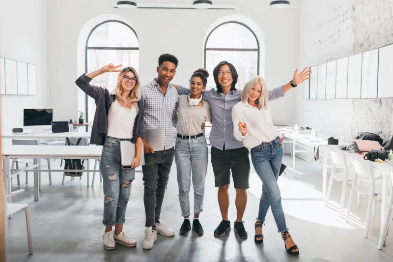 Full-length portrait of slim female office worker in jeans standing with legs crossed near asian colleague. indoor photo of tall african student and glad European woman with laptop. Free Photo