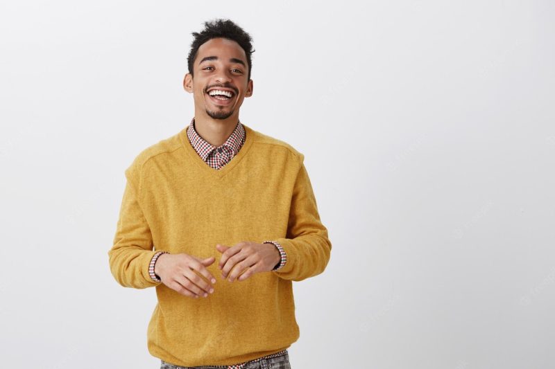 Funny friend tells hilarious jokes. indoor shot of pleased happy African-American in stylish outfit smiling broadly and gesturing over chest during conversation, having nice talk with coworker Free Photo