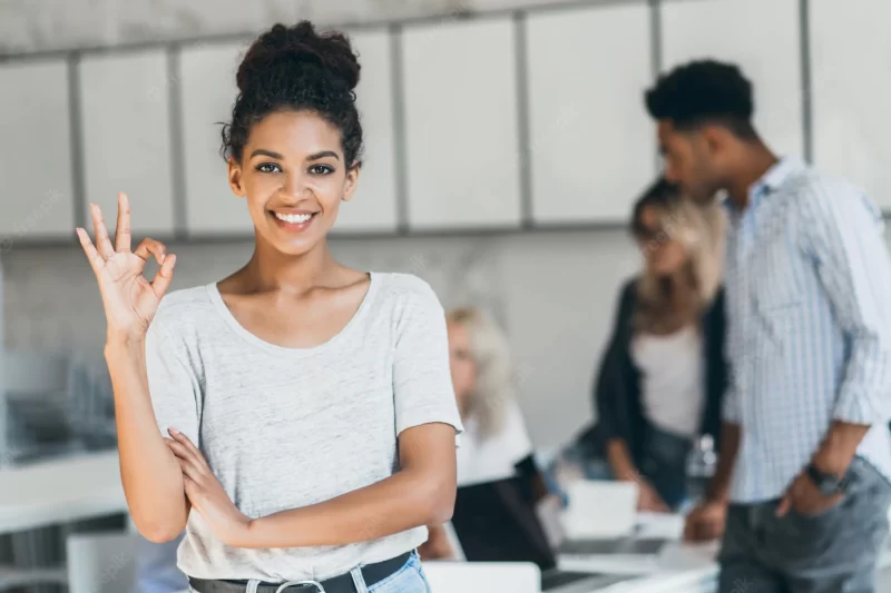 Glad african office worker with light-brown skin showing okay sign after conference with foreign partners. portrait of female black freelancer enjoying successful project. Free Photo