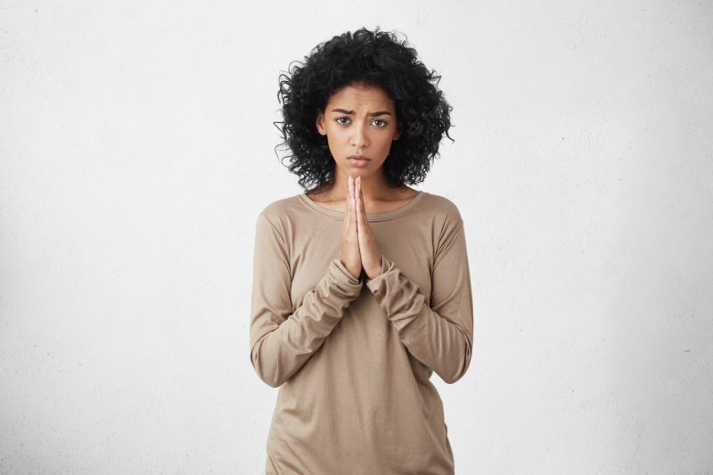 Good looking woman dressed casually keeping palms pressed together in front of her, having regretful and sorry look, begging for forgiveness. human facial expressions, emotions and body language Free Photo