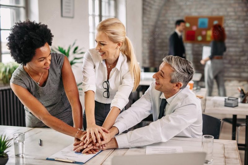 Group of happy business colleagues holding hands in unity after successful job there are people in the background Free Photo