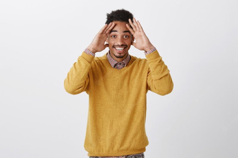 Guy did not expact to see long time friend on b-day party. thrilled pleased dark-skinned male student with afro hairstyle holding palms on forehead and smiling broadly, being surprised pleasantly Free Photo