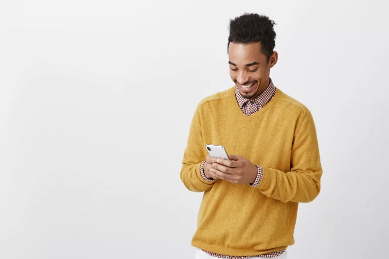 Guy met funny girl in social network. portrait of pleased happy african-american male, smiling broadly while looking at screen of smartphone, typing message or watching hilarious video Free Photo