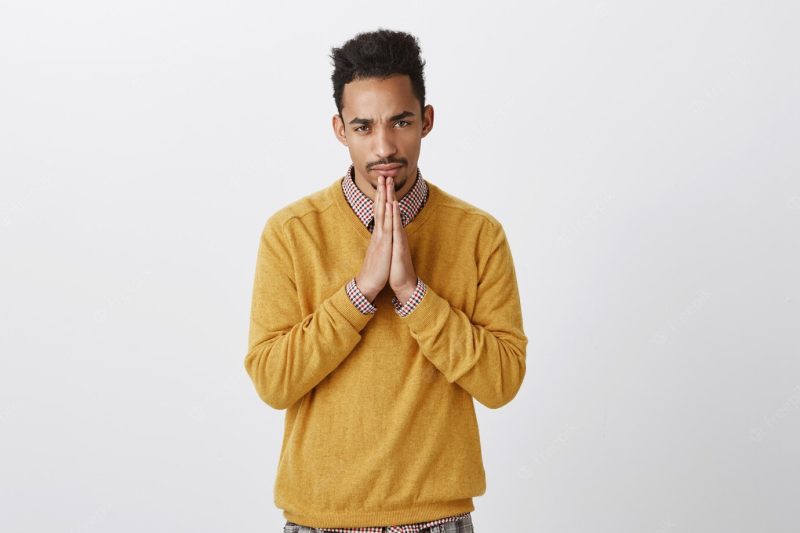 Guy trying to concentrate and calm feelings down. indoor shot of focused serious young man with fro hairstyle holding clasped hands above chin, squinting while taking work seriously Free Photo