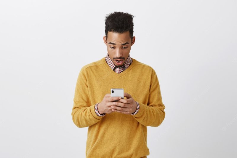 Guy typed his symptoms in internet, feeling shocked. portrait of excited amazed dark-skinned male with afro hairstyle, dropping jaw and gasping, losing speech while reading message in smartphone Free Photo