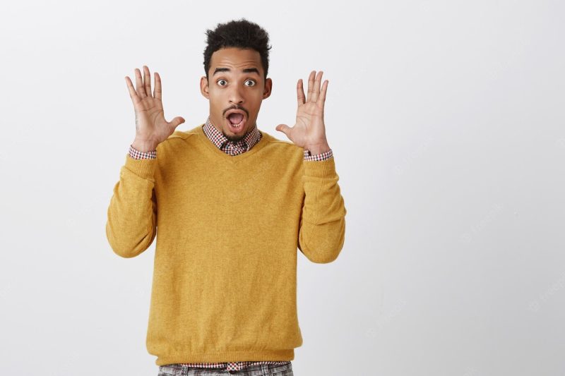 Guy was scared from unexpacted bang. portrait of attractive funny African-American with Afro hairstyle raising palms near face, shouting from surprise and amazement, dropping jaw and gasping Free Photo