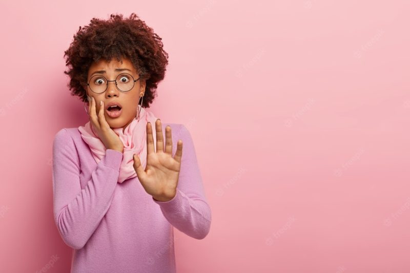 Half length shot of scared African American woman keeps palm outstretched, stares with fear, afraid of something terrible Free Photo