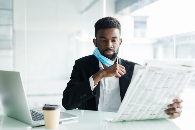 Handsome African businessman wear in medical mask with newspaper in the morning near business centre office Free Photo