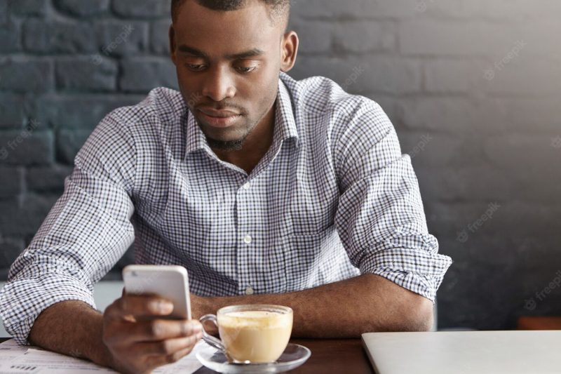 Handsome African office worker wearing checkered shirt with rolled up sleeves enjoying online communication Free Photo