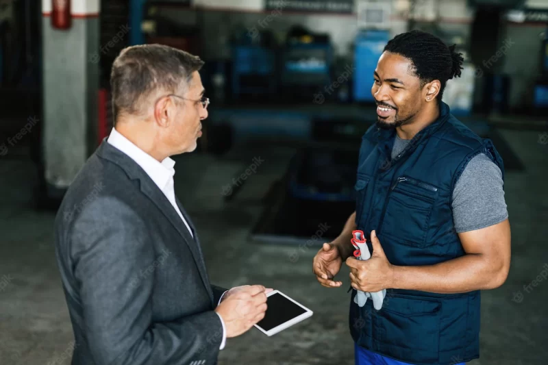 Happy african american auto mechanic talking to a customer in a repair workshop Free Photo