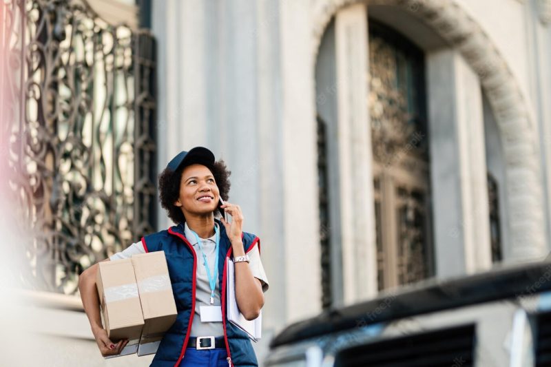 Happy African American delivery woman carrying packages and talking on mobile phone on the street Free Photo