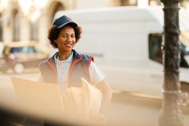 Happy african american delivery woman delivering packages and looking at the camera Free Photo