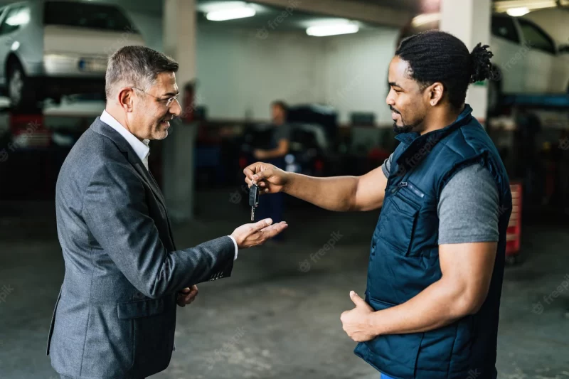 Happy african american mechanic giving car key to is customer in auto repair shop Free Photo