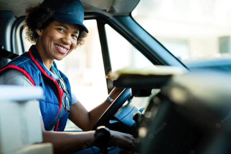 Happy black female courier driving delivery van and looking at camera Free Photo