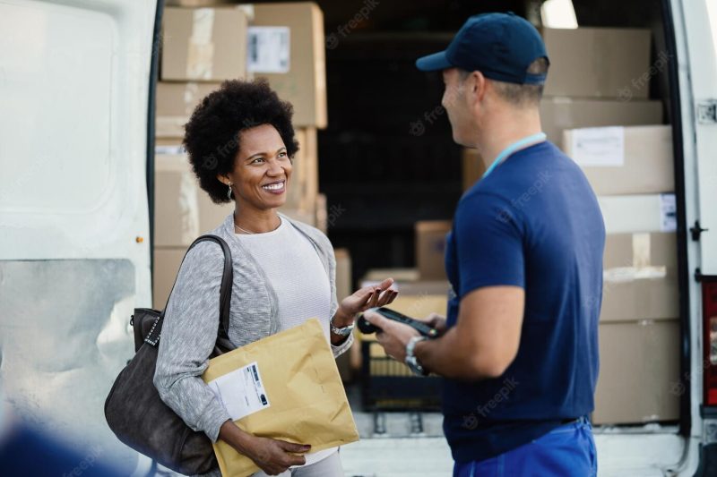 Happy black woman communicating with a courier while getting her package delivered Free Photo