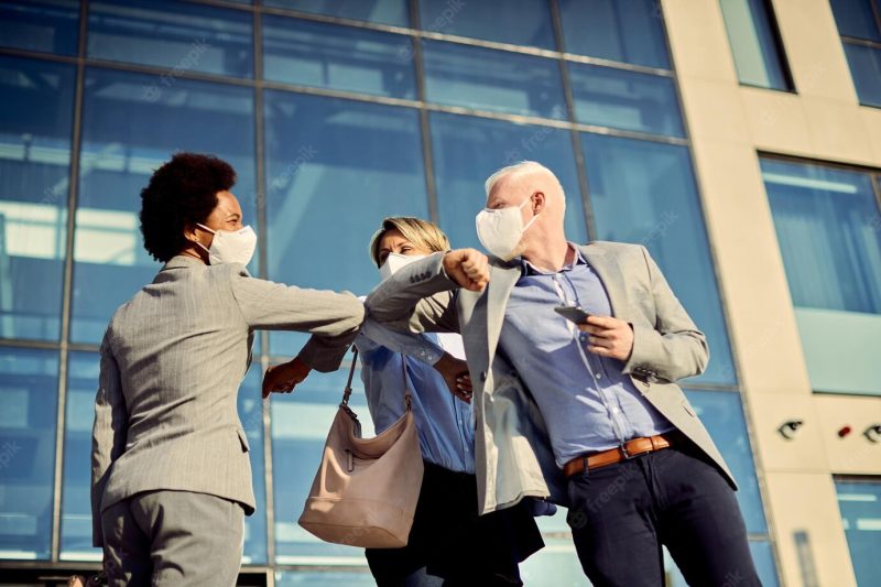 Happy business colleagues with face masks elbow bumping while greeting outdoors Free Photo