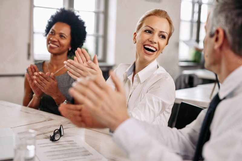 Happy businesswoman and her coworkers clapping hands on a meeting in the office Free Photo