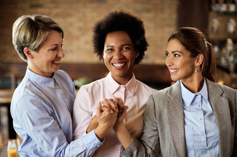 Happy businesswomen supporting each other and holding hands in a cafe Free Photo