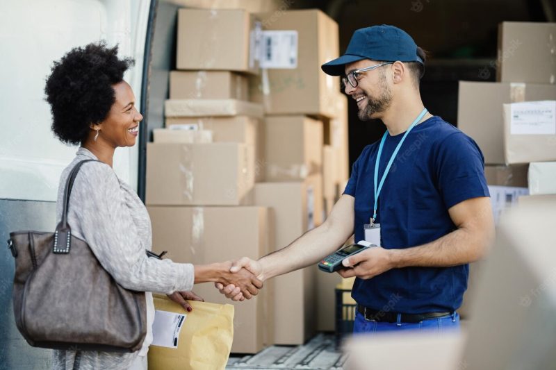 Happy courier handshaking with African American woman while delivering her a package Free Photo