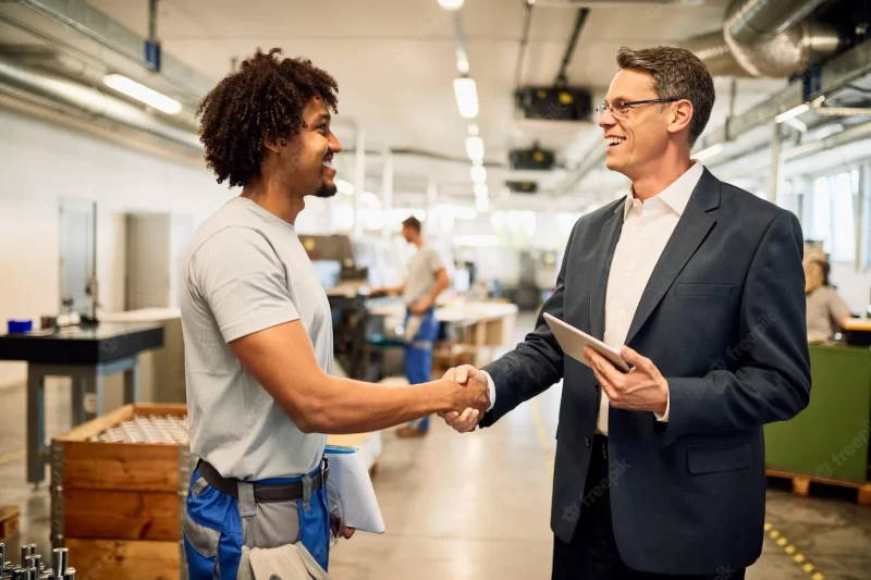 Happy engineer and young black worker handshaking while greeting in industrial building Free Photo