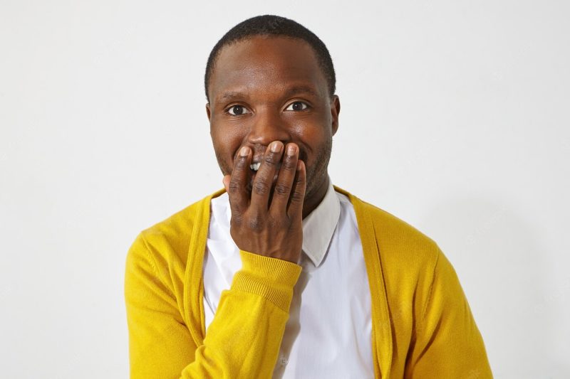 Happy excited dark skinned male covering mouth with hand, can’t believe astonishing positive news. portrait of emotional attractive african guy wearing stylish clothes smiling excitedly Free Photo