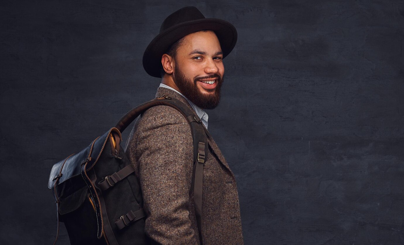 Happy Handsome Afro American Traveler Brown Jacket Hat With Backpack Stands Studio Isolated Dark Background 613910 6590