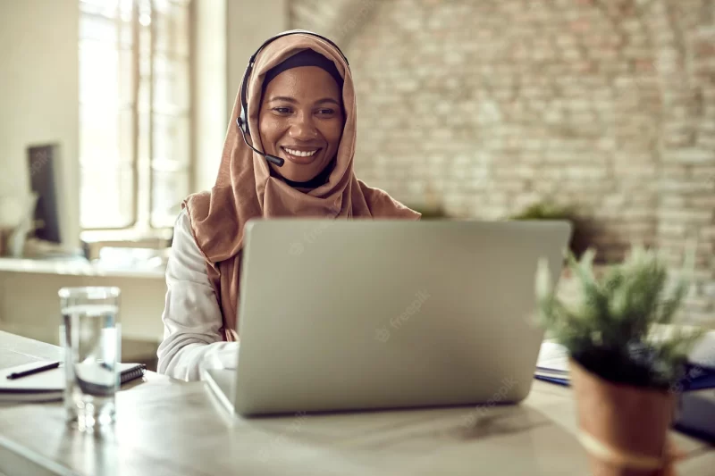 Happy islamic businesswoman working on a computer and communicating over headset in the office Free Photo