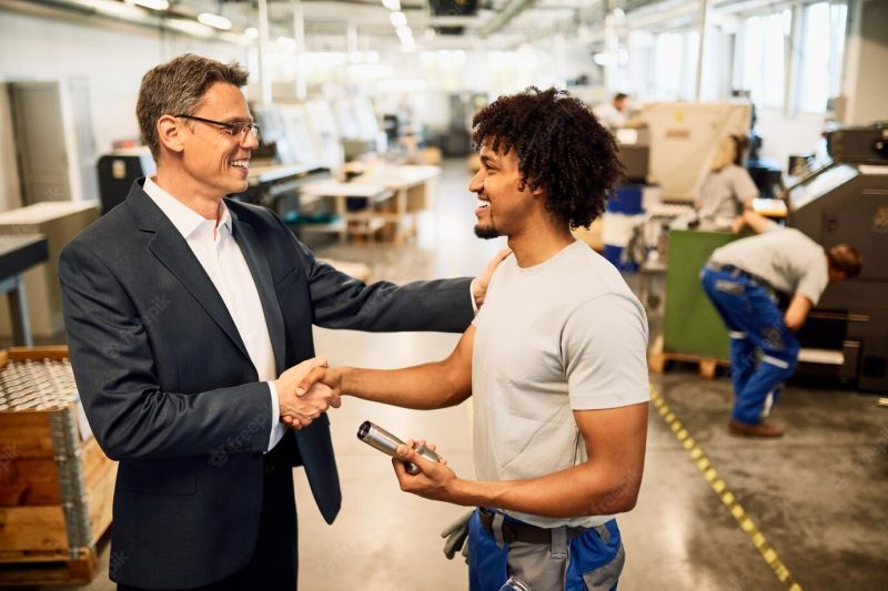 Happy manager shaking hands with African American factory worker in industrial building Free Photo