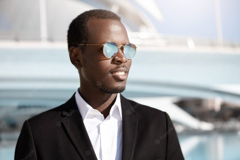 Happy successful young black employee in stylish formal wear and sunglasses looking cheerful, rejoicing at his career goals Free Photo