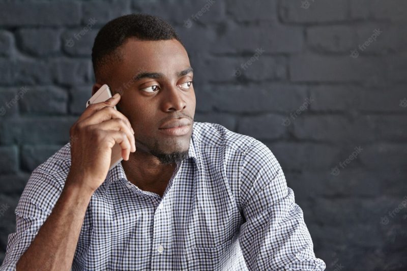 Headshot of attractive young office worker in formal wear having serious phone conversation with his boss Free Photo